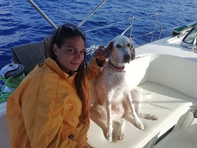 Crew member in a yellow oilskin jacket with a dog on the deck of a sailing yacht