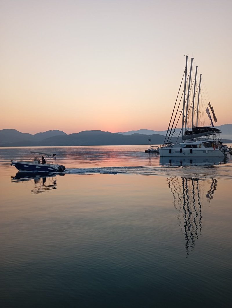 Catamaran at anchor on a mirror-calm sea at sunrise with a tender crossing the bay, Ionian Sea, Greece