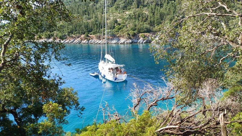 Yacht anchored alone in an emerald green bay framed by trees on a Greek sailing holiday