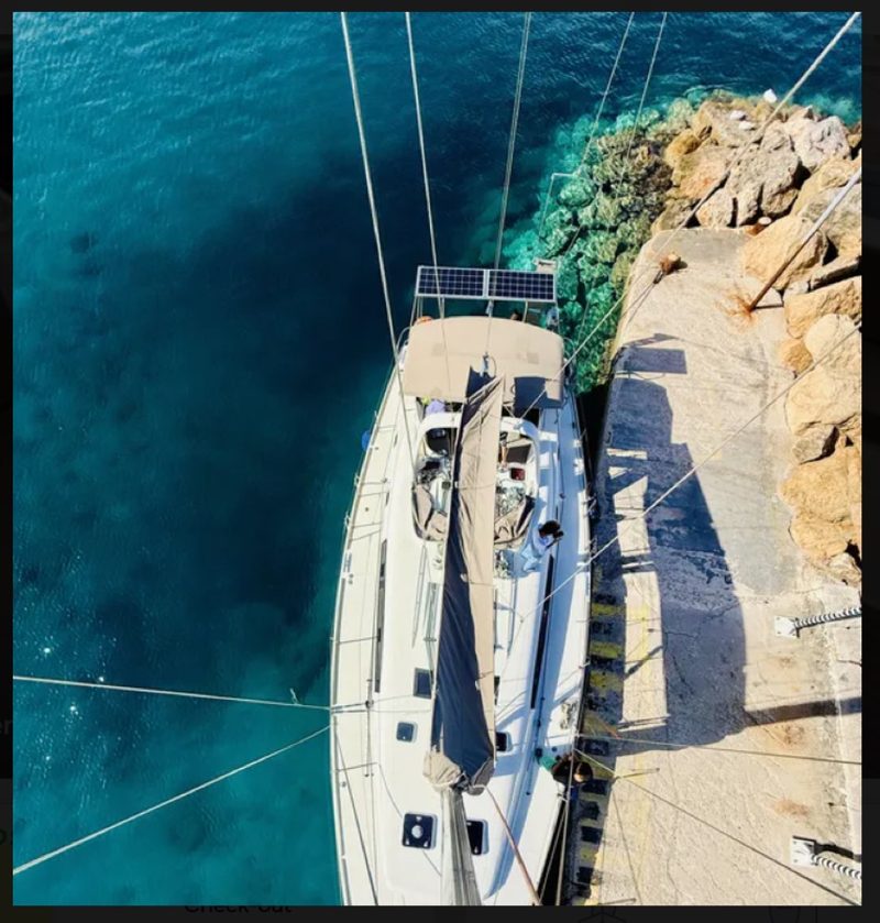 Looking down from the masthead onto a sailing yacht moored bow-to a rocky quay over turquoise water