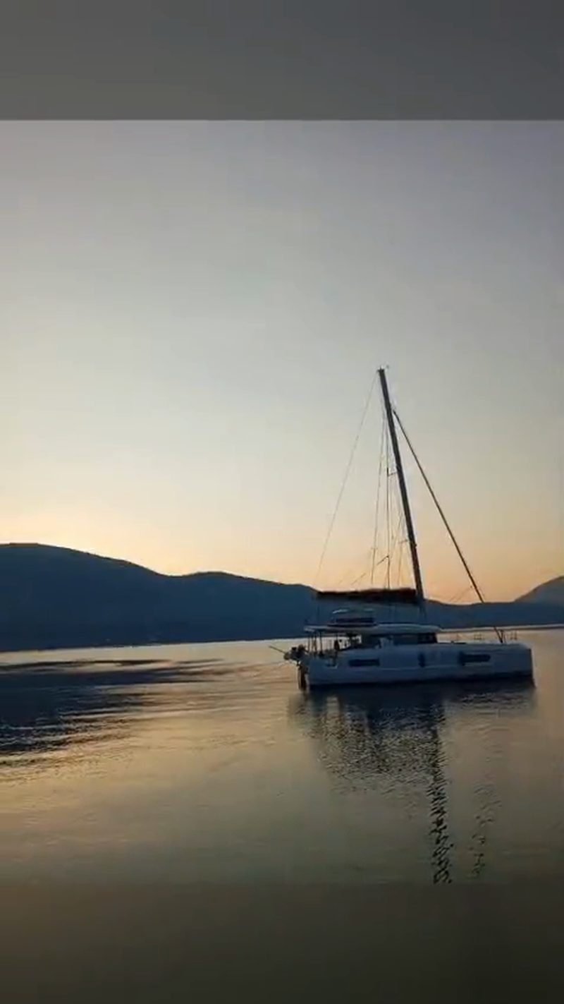 Vertical film of a catamaran at anchor on glassy water during golden hour in the Ionian Sea