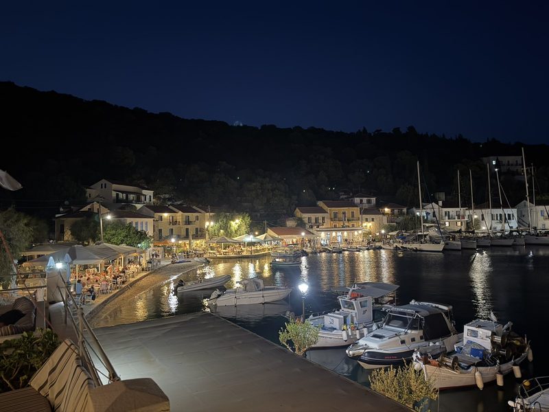 Greek island harbour at blue hour with lit tavernas along the quay and moored boats