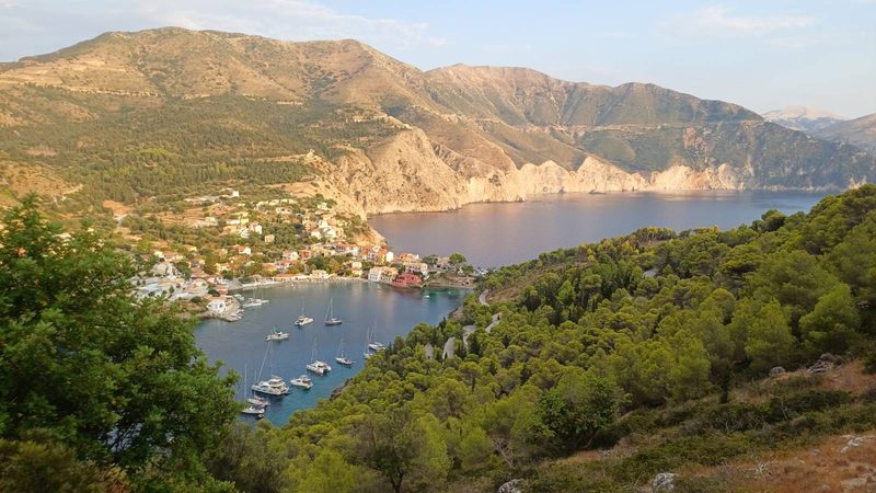 View down from a hillside over a small Greek island harbour with yachts and fishing boats at anchor