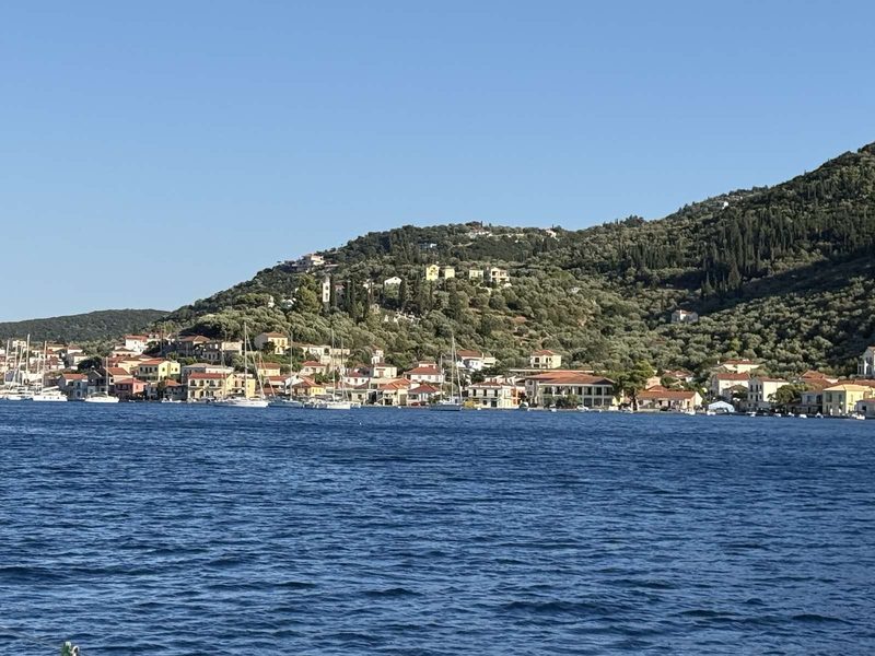 Greek island village of white and terracotta houses on a green hillside seen from a sailing yacht