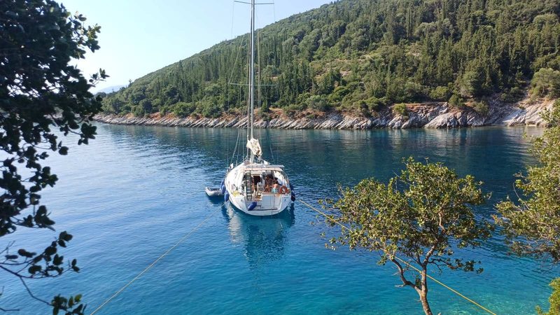 Sailing yacht at anchor in a turquoise Ionian cove framed by olive trees, on an AIyachts bareboat charter in Greece