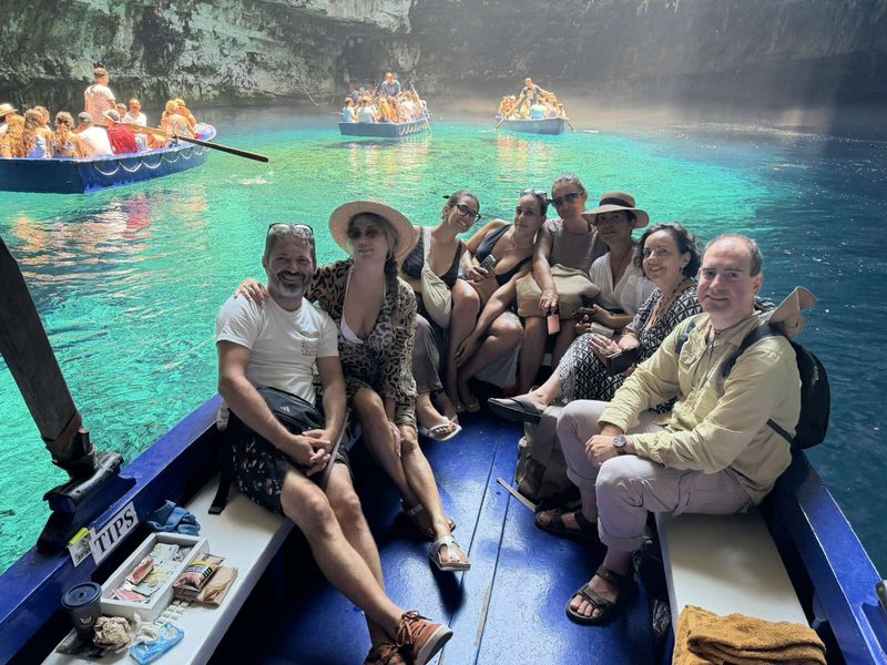 Group of AIyachts charter guests together in a boat inside a blue-lit Ionian sea cave