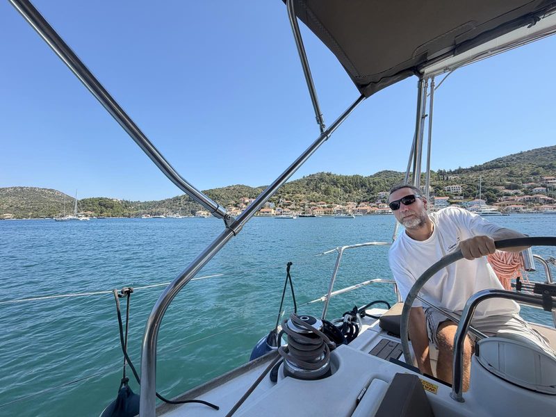 Skipper at the wheel of a charter yacht under the bimini on a bright morning in Greece