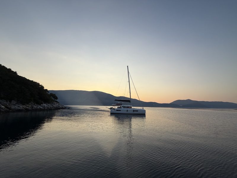Sailing yacht silhouetted at anchor on a hazy golden sea at sunset in the Ionian Islands