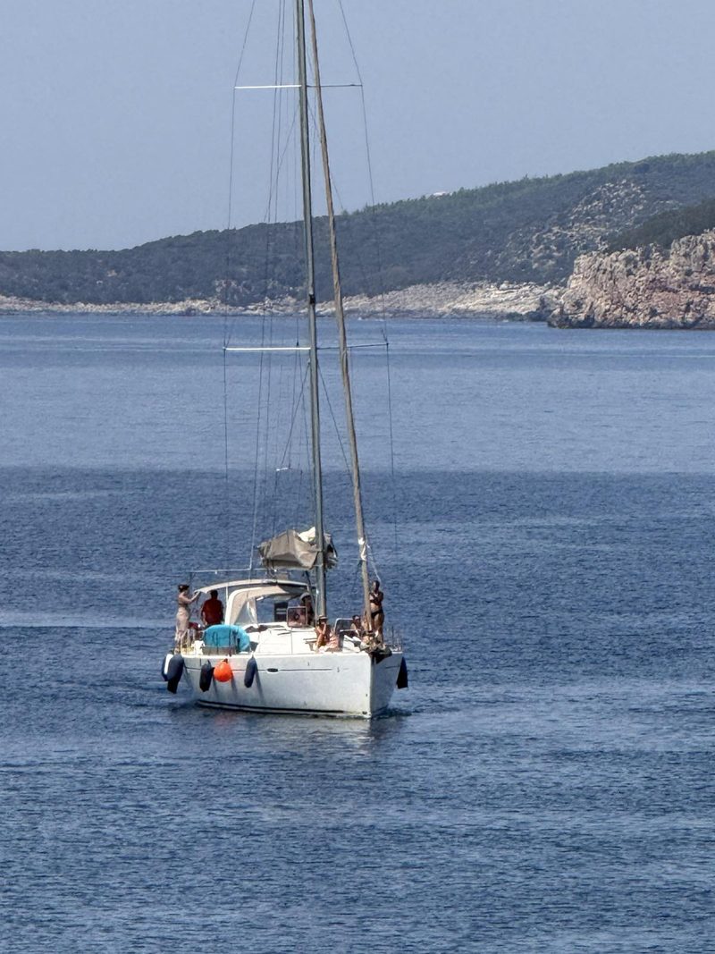 Charter sailing yacht underway with guests relaxing on the side deck, mountains of the Ionian behind